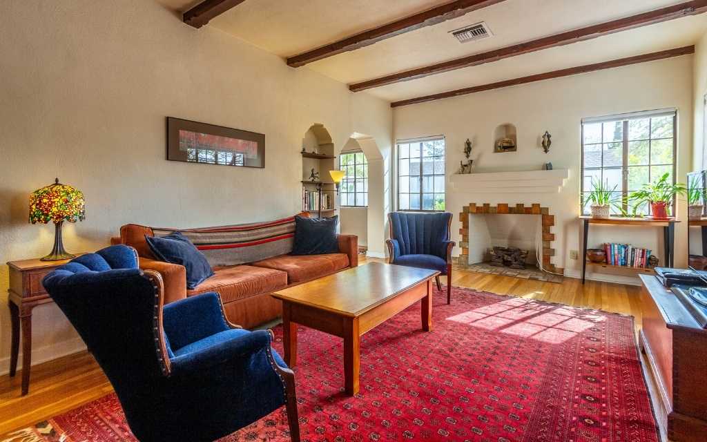Living room of a Pueblo Revival home in Sam Hughes with a vintage fireplace flanked by steel casement windows on either side. 