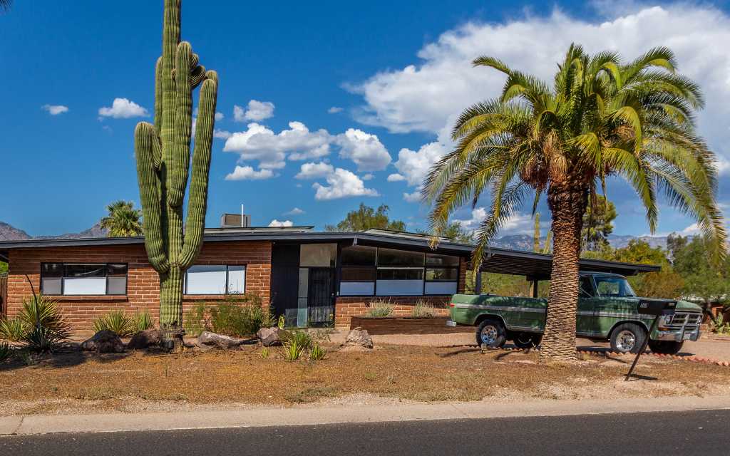 Mid century modern style home built of burnt adobe by Lusk Homes in Indian Ridge Estates. This one has a large saguaro cactus in the front  yard along with a large palm tree and a vintage early 70s Ford Ranger pick up truck.