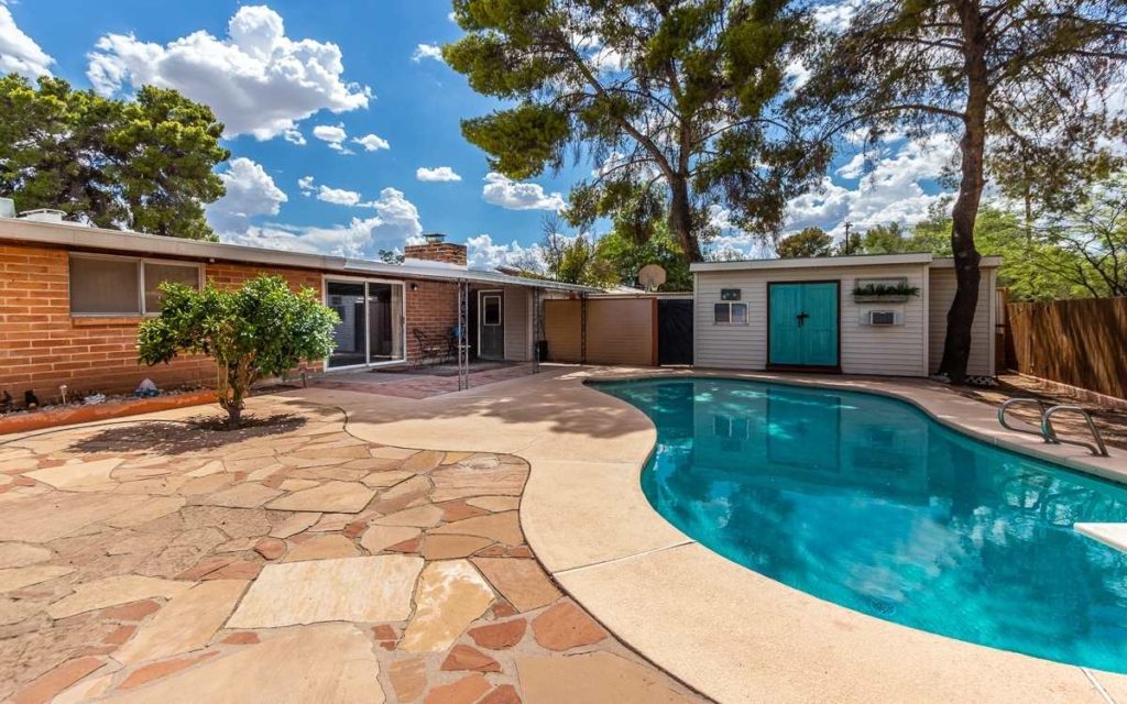 backyard view of an burnt adobe home in Tucson with a pool and a flagstone patio