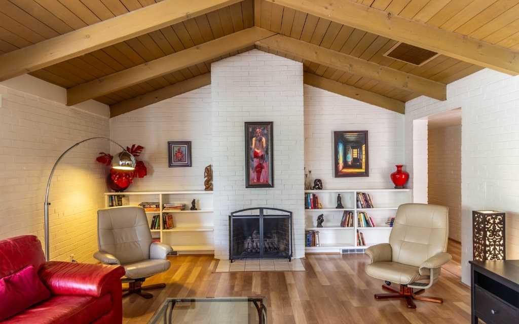 Living room of a home designed by architect Arthur Brown featuring a vaulted wood beam ceiling along with a wood burning fireplace flanked by built-in book shelves on either side.