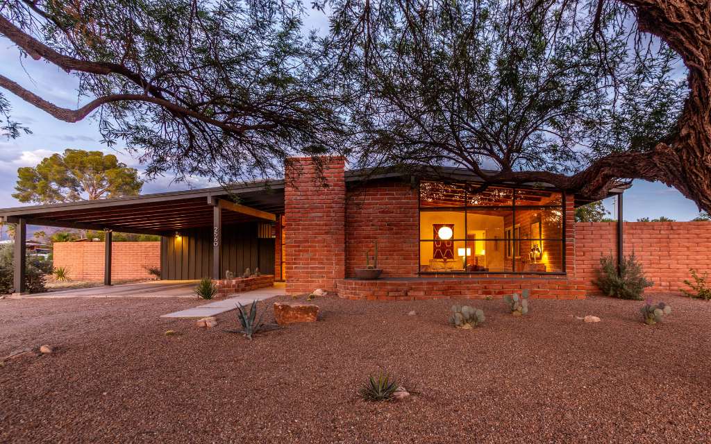 Burnt adobe midcentury modern home in Indian Ridge neighborhood in Tucson with a large angled window in the front. 