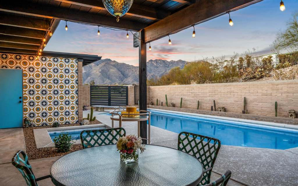 Backyard of a swanky midcentury modern home in Tucson, Arizona with a pool, and a geometric patterned tile wall behind the in-ground spa with a view of the Santa Catalina Mountain range in the background.