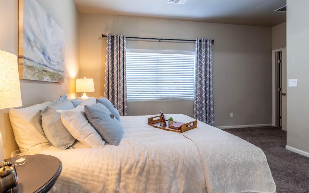 Primary bedroom after staging with a bed, curtains, nightstands, lamps, and art makes this bedroom much more iniviting.