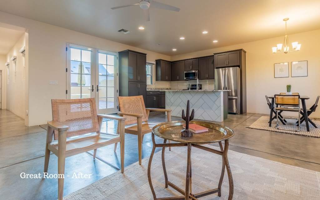 The living room of a home that's been staged featuring 2 wood chairs with a brass coffee table on a area rug in the foreground. The kitche and dining room are in the background.